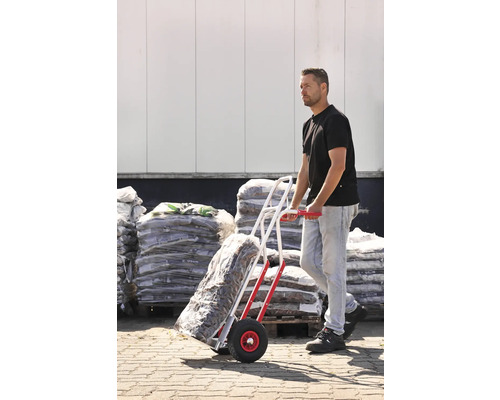 Mann transportiert Sackware mit einer Sackkarre vor einem Lager