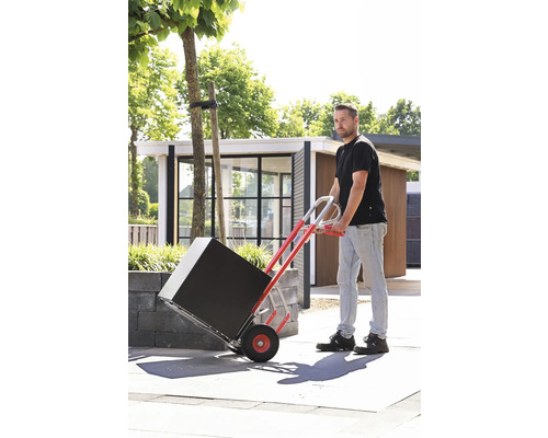 Mann transportiert schwarzes Paket mit einer Sackkarre im Freien.