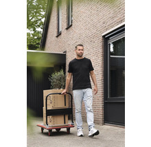 Mann transportiert Umzugskartons mit einer Transportkarre vor einem Haus.