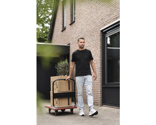 Mann transportiert Umzugskartons mit einer Transportkarre vor einem Haus.