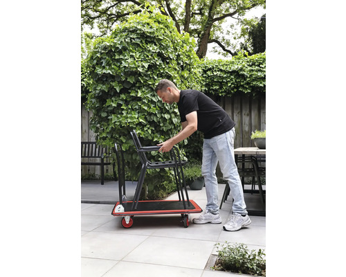 Mann transportiert Stühle auf einem Rollbrett im Garten
