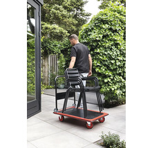 Eine Person transportiert mit einem Rollbrett Stühle im Garten.