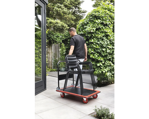 Eine Person transportiert mit einem Rollbrett Stühle im Garten.