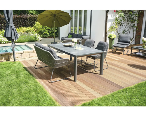Gartenszene mit Esstisch, Stühlen, Sonnenschirm und Terrasse auf Rasenfläche.