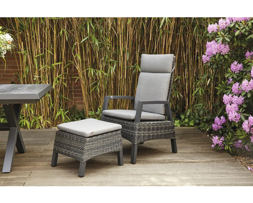 Gartenszene mit Rattansessel, Fußhocker und Tisch auf einer Holzterrasse