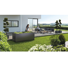 Gartenszene mit Frau beim Bepflanzen eines Hochbeets, einer Sitzecke und dekorativen Pflanzenkübeln auf einer Terrasse.