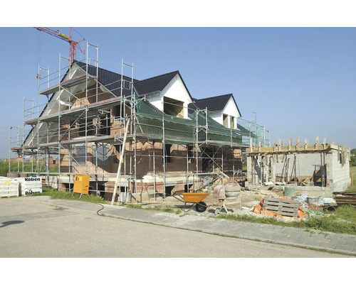 Neubau eines Hauses mit Gerüst, Zementmischer und Baumaterialien.