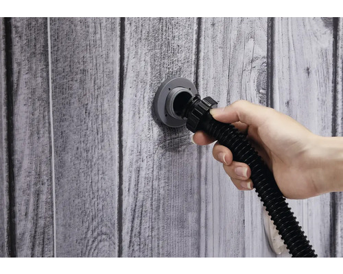 Hand schließt Schlauch an Wandanschluss an