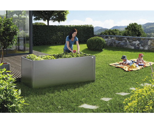 Hochbeet im Garten mit Frau bei der Ernte und spielenden Kindern