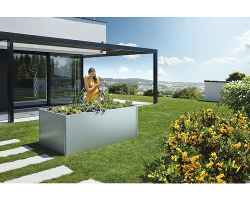 Frau gießt Pflanzen in einem erhöhten Gartenbeet im Garten.