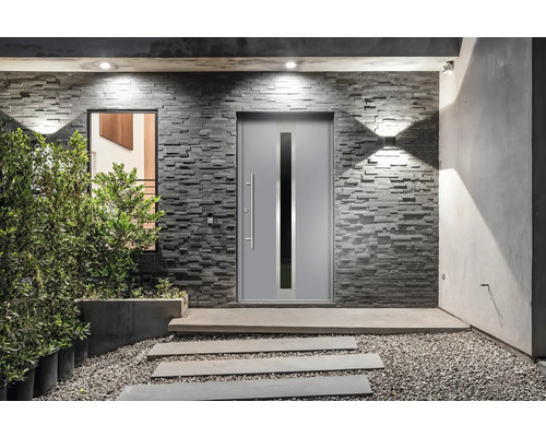 Moderne Haustür mit Glaseinsatz in einer Steinmauer mit Wegplatten