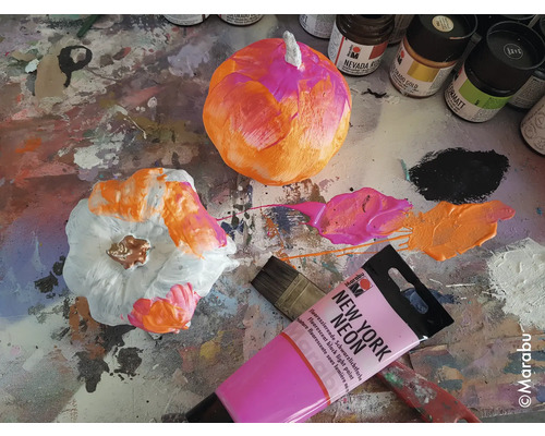 Bemalte Kürbisse mit Farben und Pinsel auf einer Arbeitsfläche.