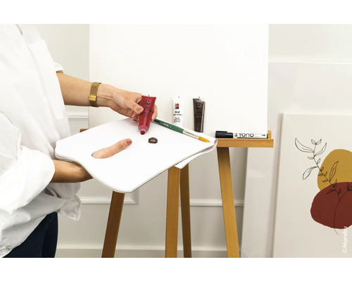 Szene mit Acrylfarben, Pinsel, Farbpalette und Leinwand auf einer Staffelei.
