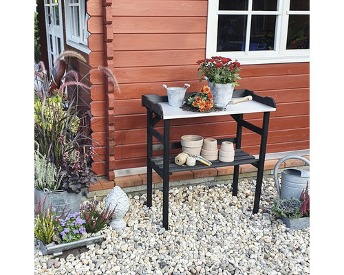 Gartenszene mit einem Gartentisch vor einem Gartenhaus, dekoriert mit Blumen und Gartenzubehör.