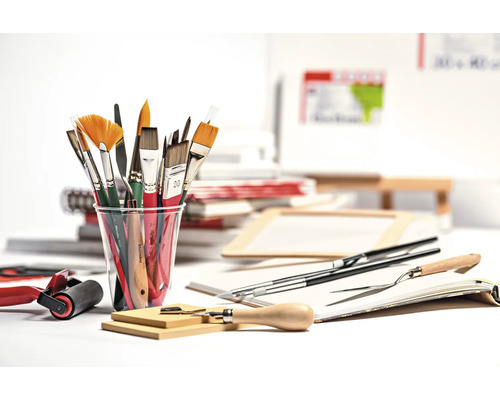 Verschiedene Pinsel in einem Becher sowie weitere Malutensilien auf einem Tisch