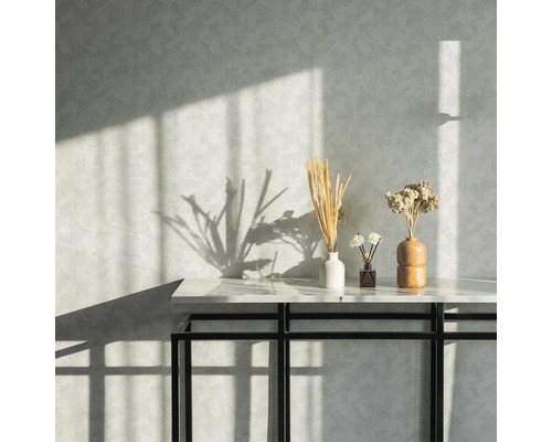 Dekorative Trockenblumen in Vasen auf einem Tisch vor einer strukturierten Wand mit Schatten.
