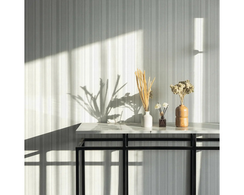 Dekorative Trockenblumen in Vasen auf einem Tisch vor einer gestreiften Wand.