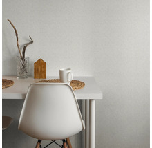 Szene mit strukturierten Tapeten an der Wand, einem Tisch, einem Stuhl, einem Glas, einem Holzhaus und einer Tasse