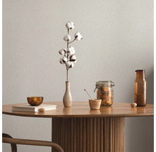 Dekoratives Arrangement auf einem Holztisch mit Geschirr und einer Baumwollblume in einer Vase.