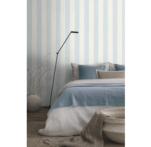 Schlafzimmer mit Bett, Stehlampe und gestreifter Tapete für eine helle Atmosphäre.