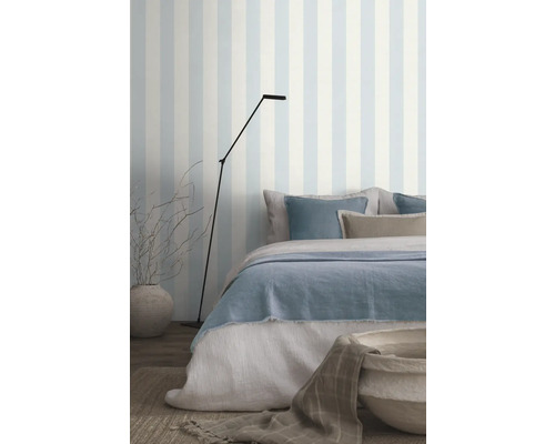 Schlafzimmer mit Bett, Stehlampe und gestreifter Tapete für eine helle Atmosphäre.