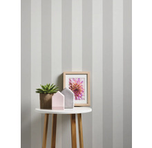 Dekoratives Interieur mit gestreifter Tapete, Tisch, Pflanze, Bilderrahmen und Dekoration.