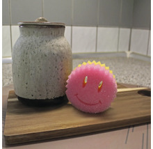 Keramikdose mit Deckel und ein Spülschwamm mit Smiley-Gesicht auf einem Holzbrett