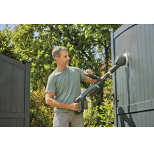 Mann reinigt Tor mit elektrischer Bürste im Garten.