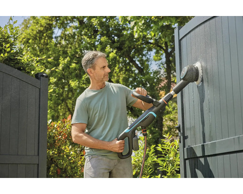Mann reinigt Tor mit elektrischer Bürste im Garten.
