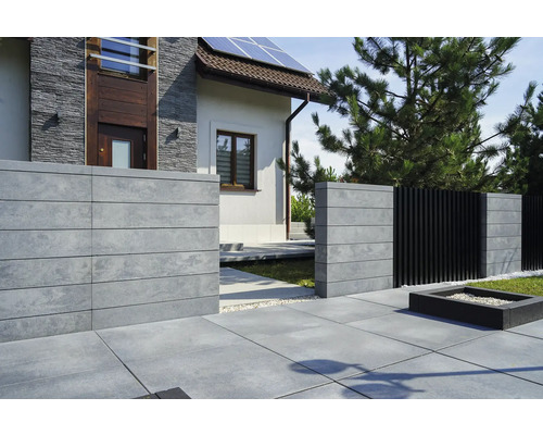 Außenansicht eines Hauses mit Betonzaun und Steinplattenweg