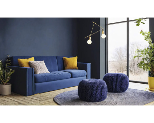 Wohnzimmer mit blauem Sofa, Zierkissen, runden Hockern und Zimmerpflanzen