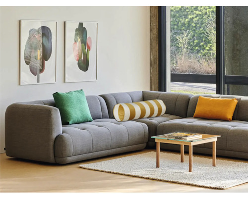 Wohnzimmer mit grauer Eckcouch, Kissen, Tisch und Bildern an der Wand.