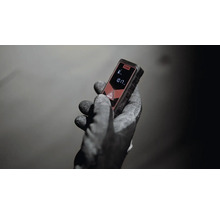 Hand mit Arbeitshandschuh hält einen Laser-Entfernungsmesser.