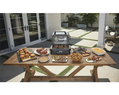 Tisch mit Speisen und offenem Grill im Außenbereich.