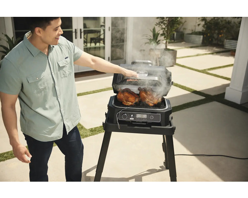 Mann grillt zwei Hähnchen mit einem elektrischen Ninja Grill im Freien.