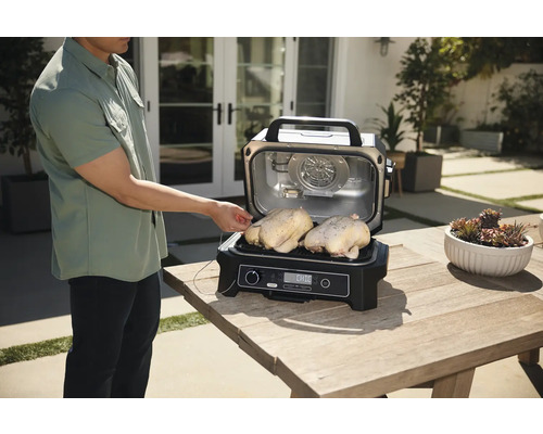 Person prüft die Temperatur von zwei Hähnchen auf einem Ninja Grill im Freien.