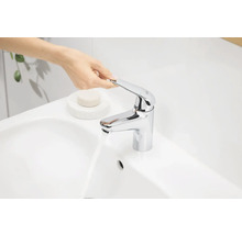 Person bedient einen verchromten Waschtischmischer an einem Waschbecken.