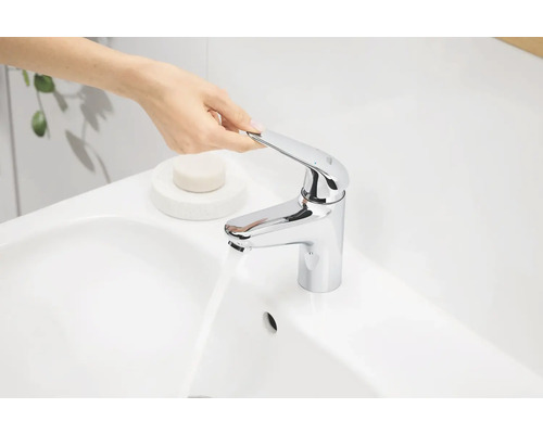 Person bedient einen verchromten Waschtischmischer an einem Waschbecken.
