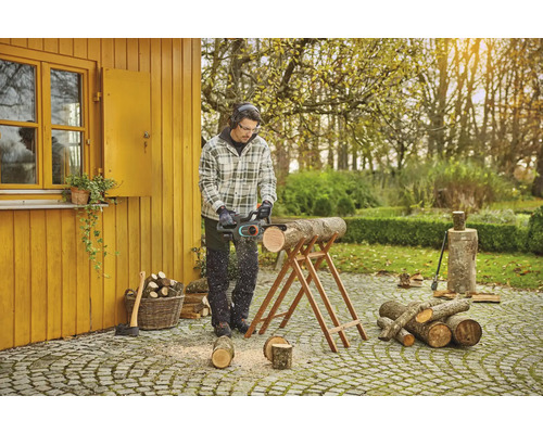 Mann sägt Holz mit einer Kettensäge im Garten.