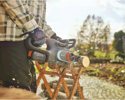 Gartenarbeiter sägt Holzscheit mit Akku-Kettensäge auf einem Sägebock im Garten.