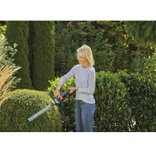 Frau schneidet Hecke mit Heckenschere im Garten.