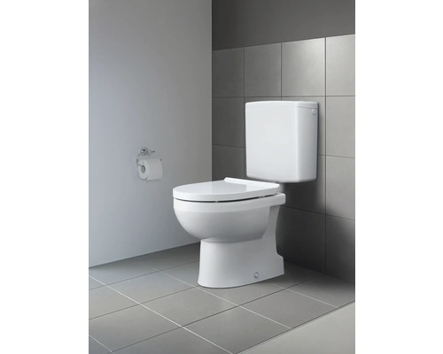 Weisse Toilette mit Aufputzspülkasten vor grauer Wandfliese und Toilettenpapierhalter