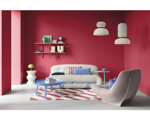 Wohnzimmer mit Sofa, Sessel, Teppich, Tisch und Regalen vor roter Wand