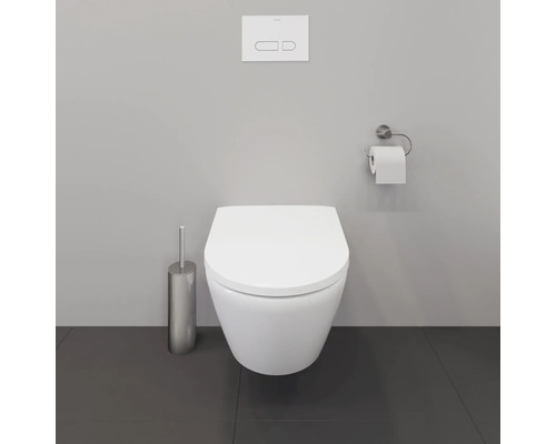 Wandhängendes Tiefspülklosett mit Betätigungsplatte, Toilettenpapierhalter und WC-Bürstengarnitur in einem Badezimmer.