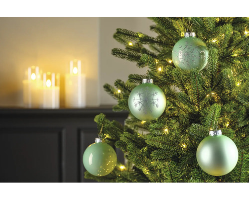 Nahaufnahme eines Weihnachtsbaums mit grünen Kugeln und Lichtern, im Hintergrund Kerzen.