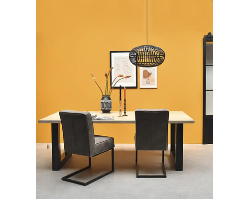 Moderner Essbereich mit einem Holztisch, schwarzen U-Beinen, zwei grauen Freischwinger-Stühlen und einer schwarzen Gitterpendelleuchte vor gelber Wand.