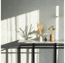 Dekorative Elemente auf einem Tisch vor einer gemusterten Wand mit Sonnenlicht.