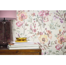 Nahaufnahme einer Wandtapete mit Blumenmuster, ergänzt durch eine Lampe, Bücher und eine Schale auf einem Holzmöbelstück.