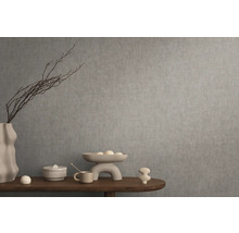 Dekoratives Stillleben mit Vase, Schale und Ziergegenständen auf einem Holztisch vor einer grauen Wand.