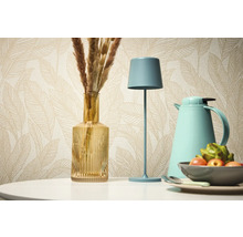 Dekoratives Stillleben mit Tischleuchte, Vase und Thermoskanne vor einer gemusterten Tapete.